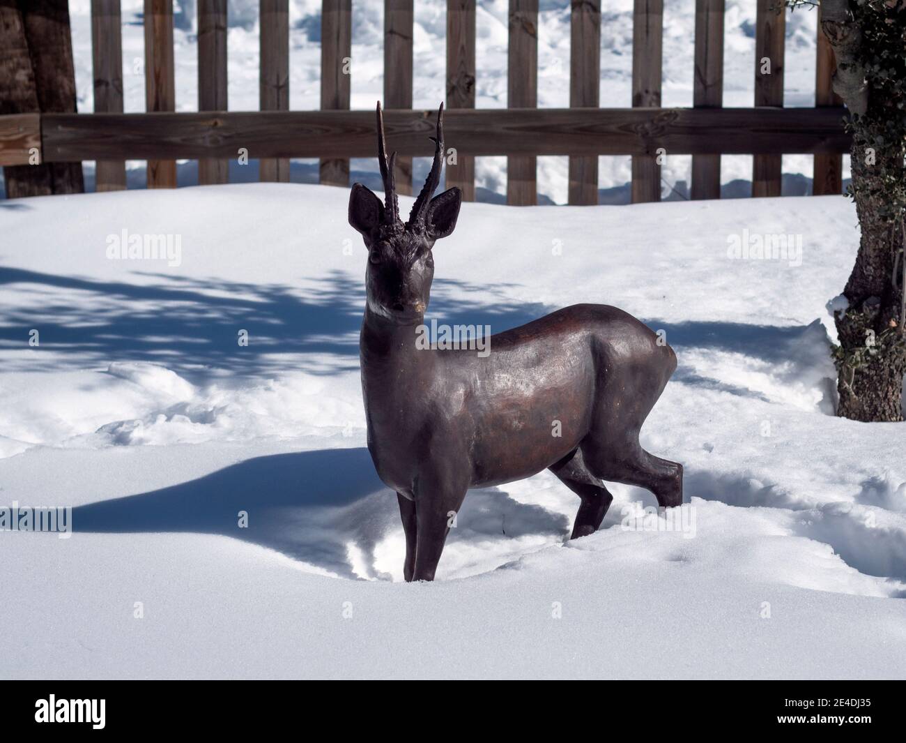 Scultura di capriolo in bronzo nella neve e recinzione in legno sullo sfondo. Foto Stock