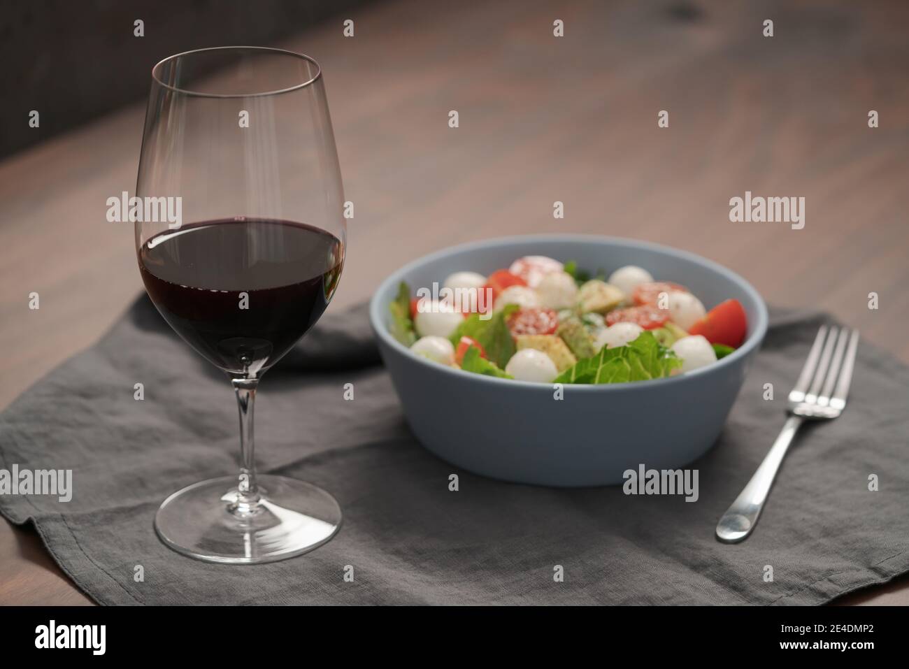 Bicchiere di vino rosso con insalata con romaine, pomodori e mozzarella in ciotola blu, a fuoco basso Foto Stock