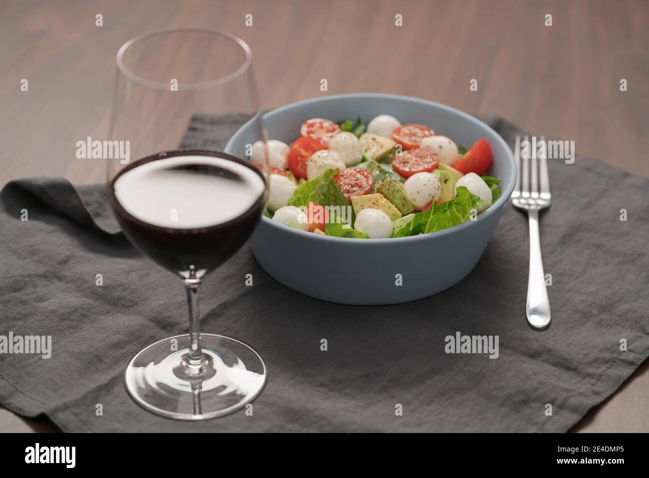 Insalata con romaine, pomodori e mozzarella in ciotola blu con bicchiere di vino rosso, a fuoco basso Foto Stock