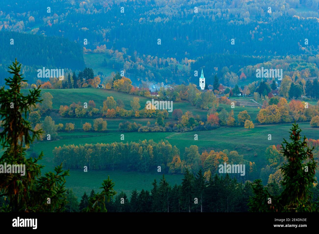 Sumava, Repubblica Ceca, serata in Kasperske hory con la chiesa,. Giornata fredda nel parco nazionale di Sumava, colline e villaggi in aranci, vista nebbiosa sulla cz Foto Stock