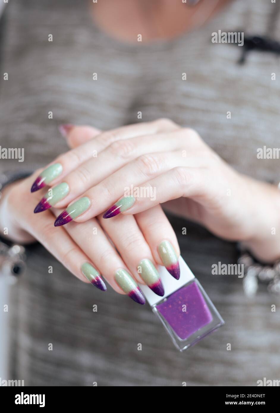Mani femminili con unghie lunghe verdi e viola e un bottiglia di smalto per  unghie Foto stock - Alamy