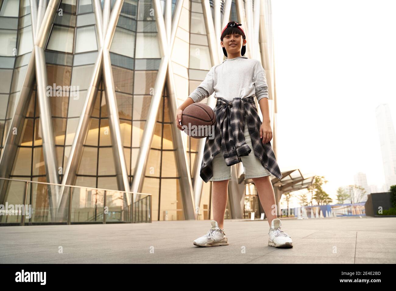 ritratto esterno ad angolo basso di un teenage basketball asiatico di quindici anni lettore Foto Stock