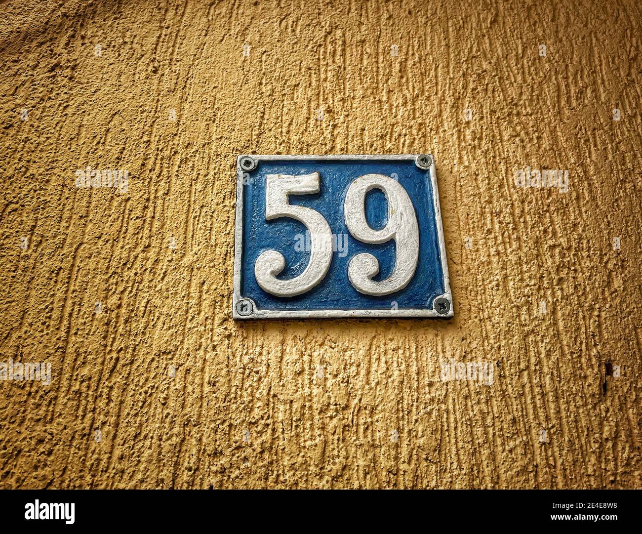 Numero 59, il numero di case, appartamenti, strade. Il numero bianco su una piastra di metallo blu, ospita il numero cinquantanove (59) su una parete ruvida. Foto Stock