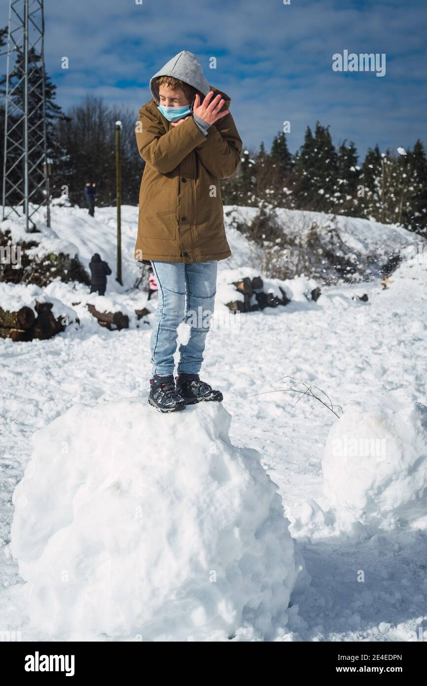 Ragazzo caucasico con una maschera in piedi su una grande palla di neve e cercando di fuggire da una palla di neve Foto Stock