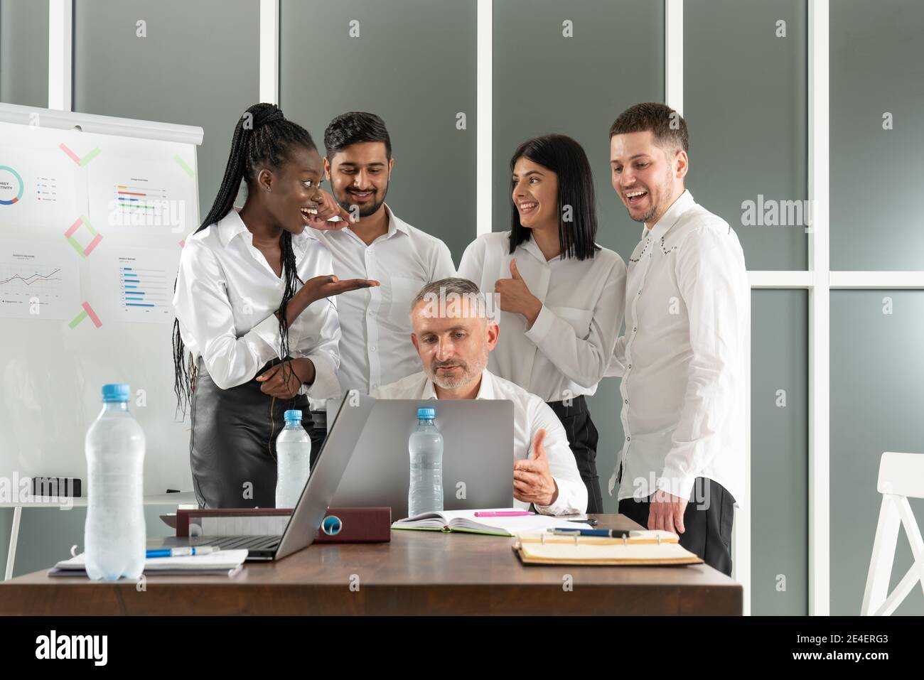 Il team leader maschile ascolta le diverse domande dei colleghi, seduti insieme al tavolo in ufficio. Gara mista giovani compagni di squadra che discutono i dettagli del progetto Foto Stock