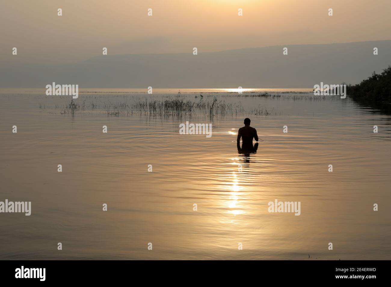 L'uomo silhouette entra nel lago di Galilea in Israele all'alba. Foto Stock