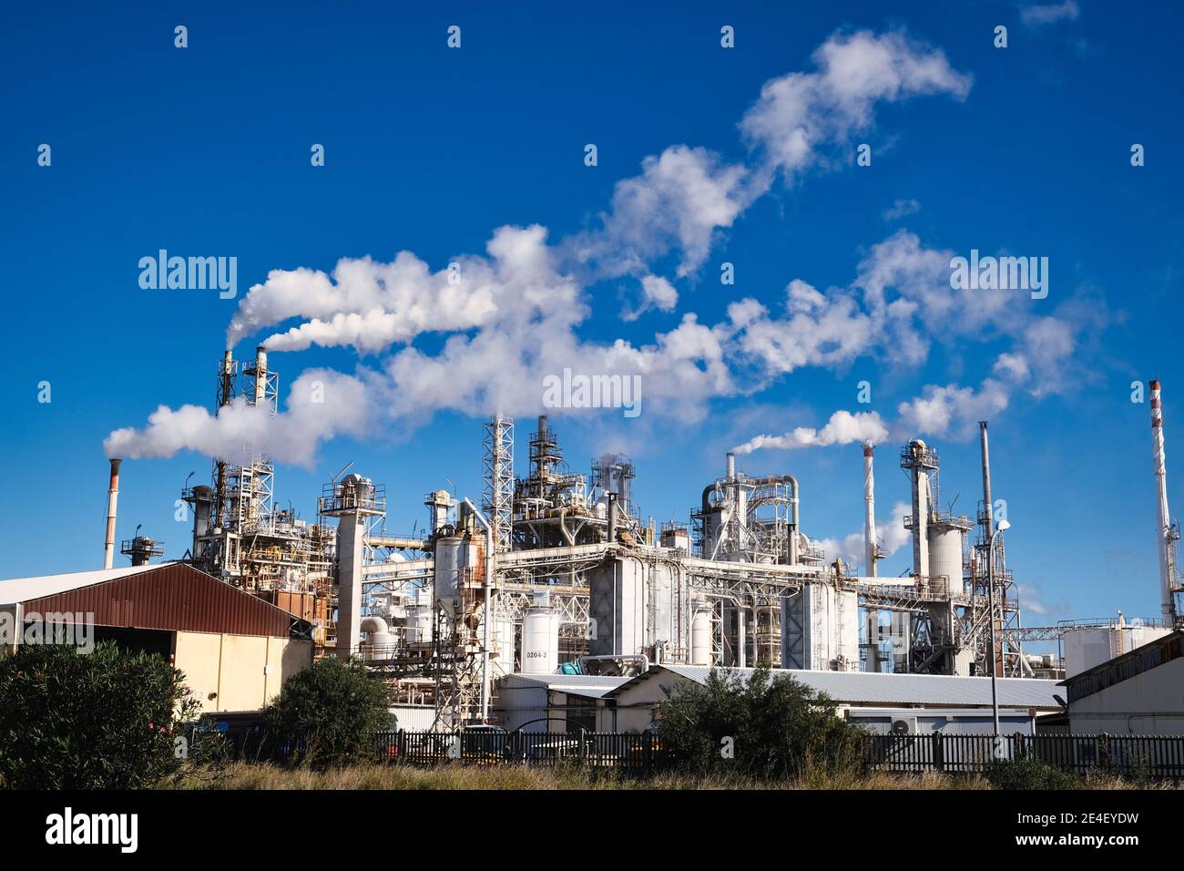 Vista di un impianto chimico con molti imbuti con fumo bianco su un cielo blu Foto Stock