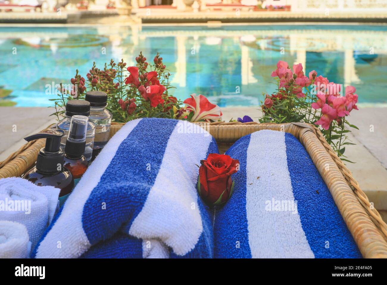 Asciugamani in rotolo e bottiglie per la cura della pelle sono sul cesto vicino a una piscina. Concetto di relax estivo Foto Stock