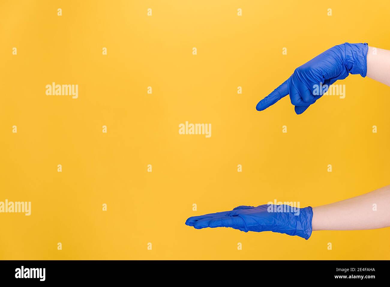 Inriconoscibile giovane femmina apertura e puntando sul palmo sul copyspace da parte, indossa guanti medici protettivi blu, isolati su sfondo giallo Foto Stock