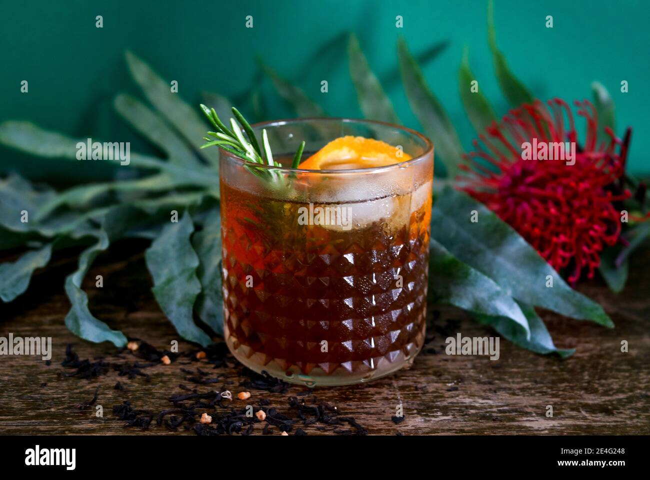 Cocktail al rum o al whisky vecchio stile davanti a uno sfondo botanico tropicale di colore verde scuro Foto Stock Cocktail al rum o al whisky vecchio stile davanti a uno sfondo botanico tropicale di colore verde scuro Foto Stock