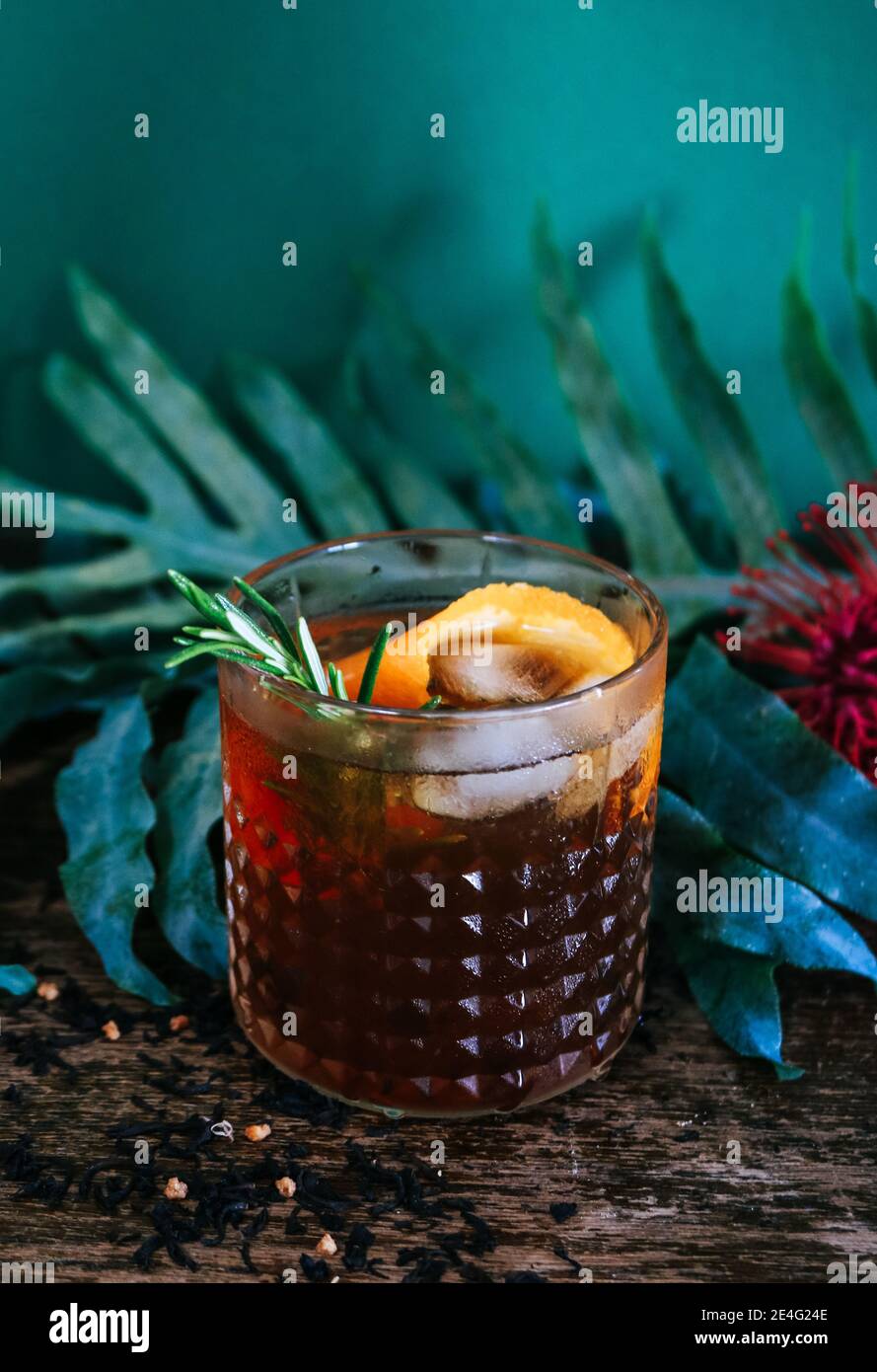 Cocktail al rum o al whisky vecchio stile davanti a uno sfondo botanico tropicale di colore verde scuro Foto Stock