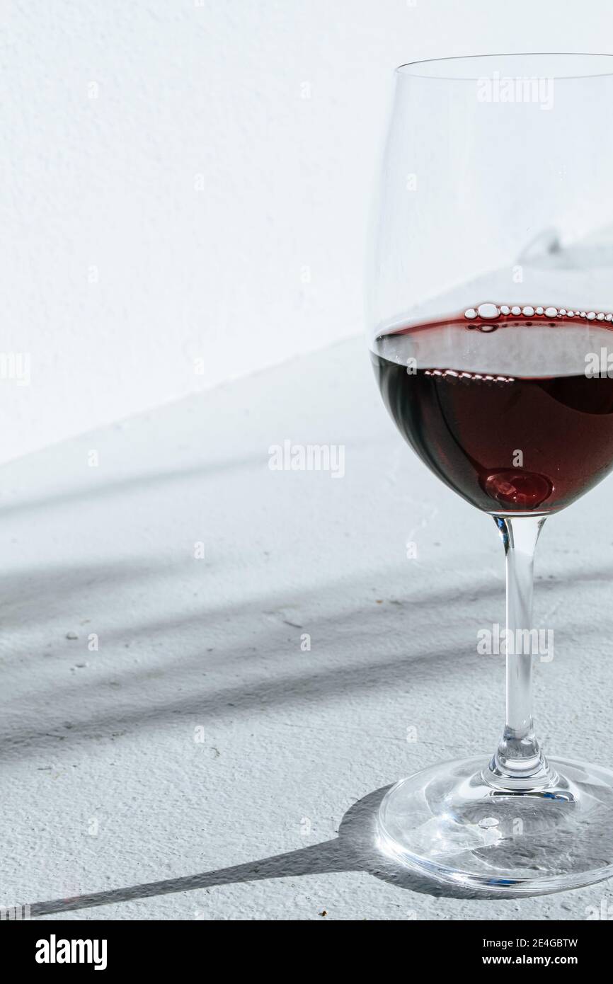 Primo piano di un bicchiere di vino rosso in piedi fronte di una parete bianca con ombre di piante in estate Foto Stock