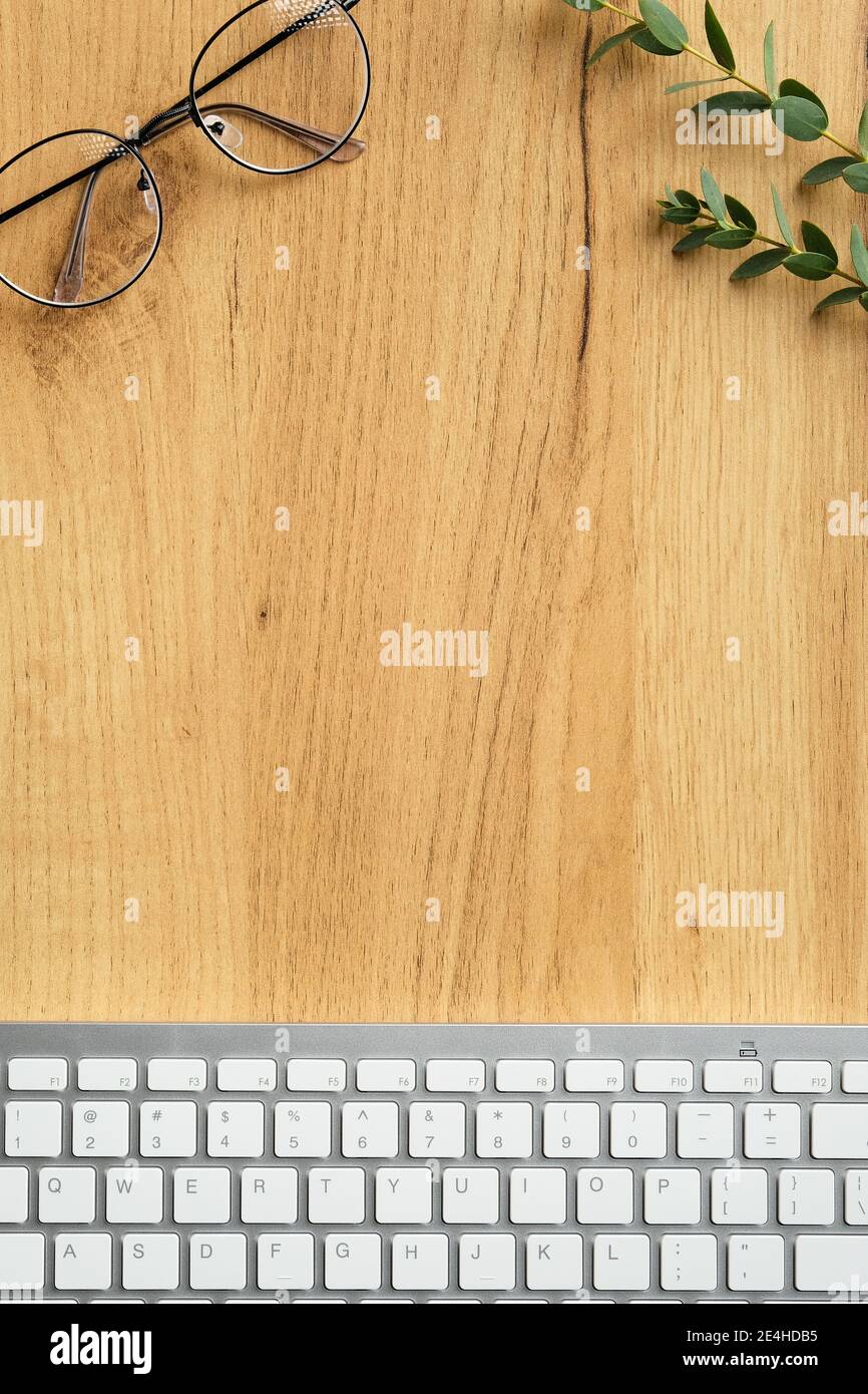 Moderno tavolo da lavoro con tastiera, bicchieri, foglie di eucalipto su sfondo di legno. Posa piatta, parte superiore vie. Stile minimalista Foto Stock