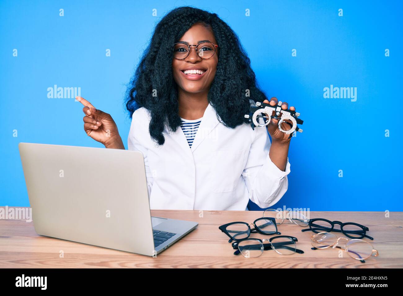 Bella donna africana che tiene occhiali di optometria sorridente felice indicando con mano e dito di lato Foto Stock