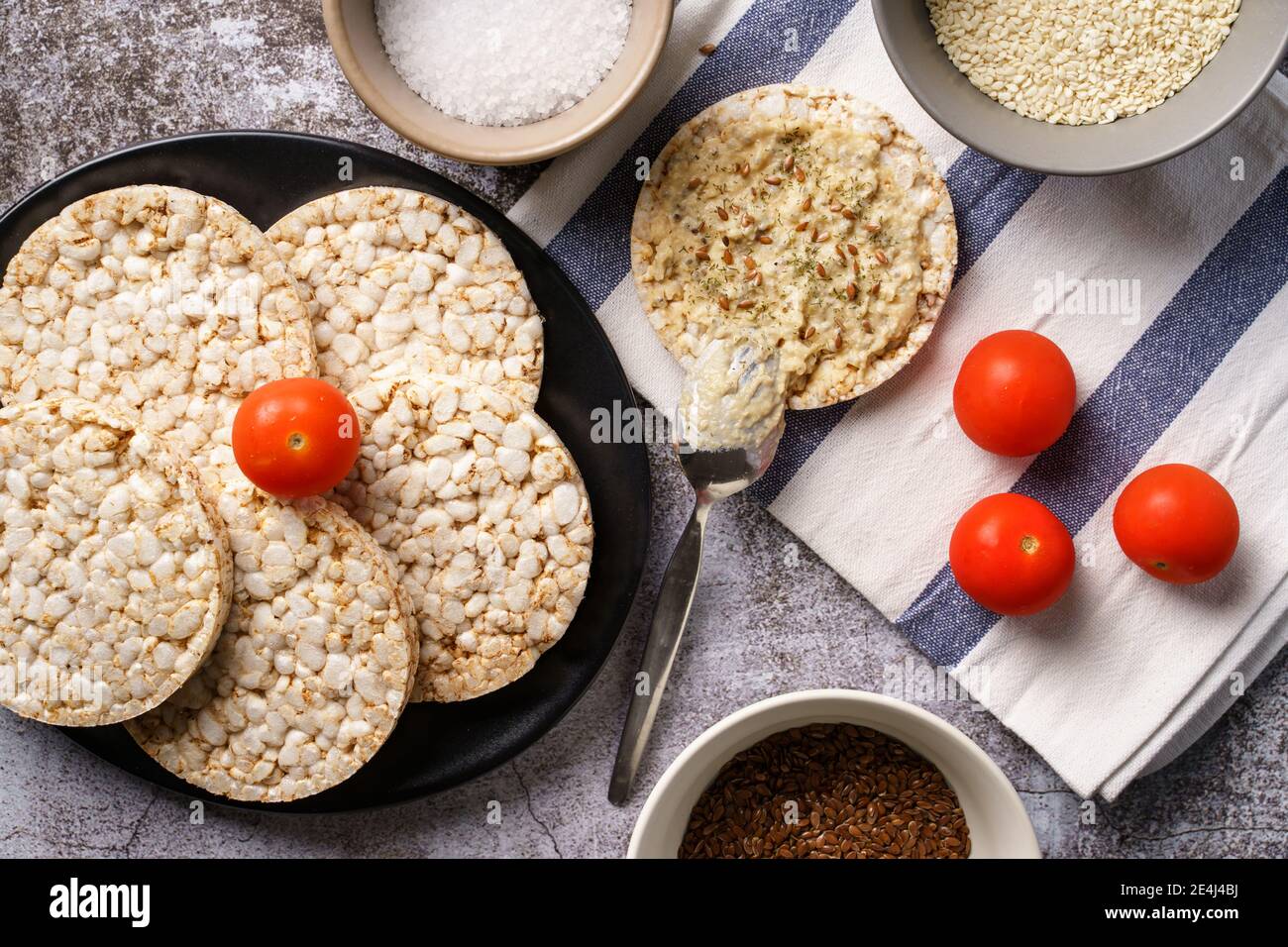 Croccanti torte di riso soffiato sul tavolo hummus spalmato e pomodoro verdure e semi di sesamo sul tavolo - vista dall'alto per una sana colazione vegetariana o vegana Foto Stock