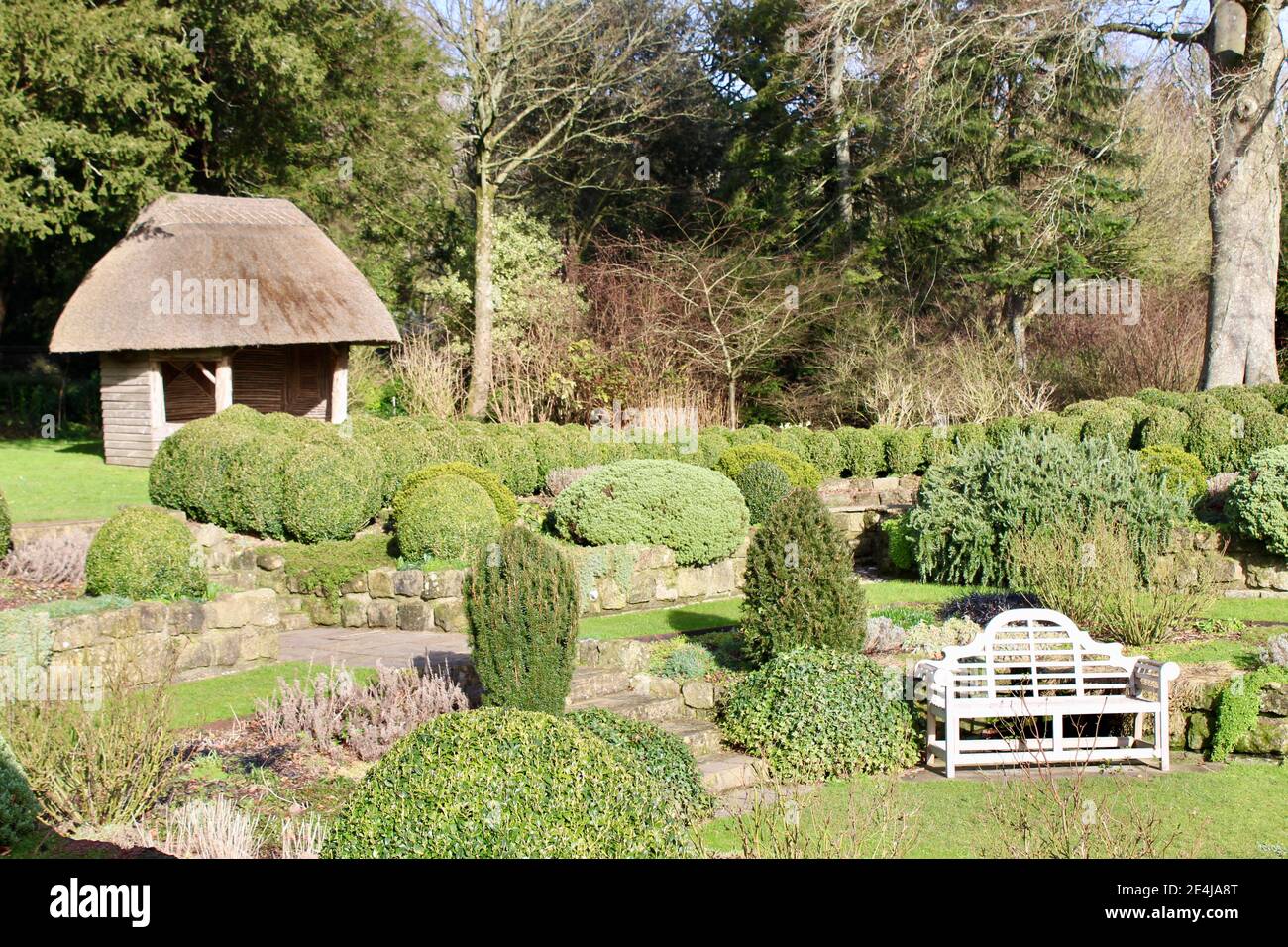 Giardino sommerso nei giardini del West Dean con posti a sedere e casa estiva rustica con tetto in paglia. West Dean, Chichester, West Sussex. Foto Stock