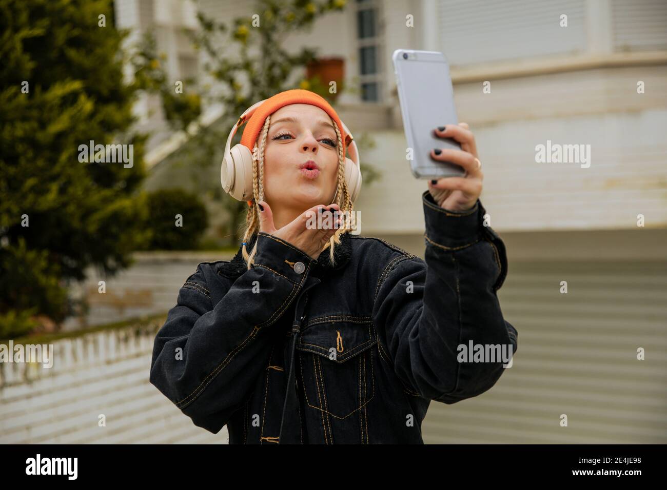 Donna alla moda che soffia bacio mentre prende selfie attraverso il telefono cellulare Foto Stock