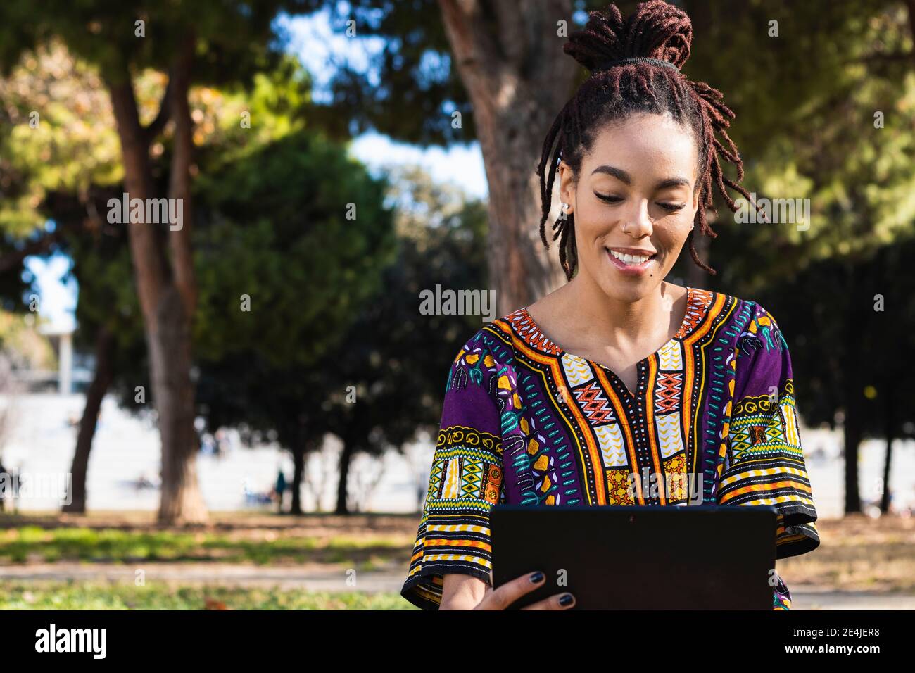 Bella donna giamaicana con Dreadlock utilizzando tablet digitale al parco il giorno di sole Foto Stock