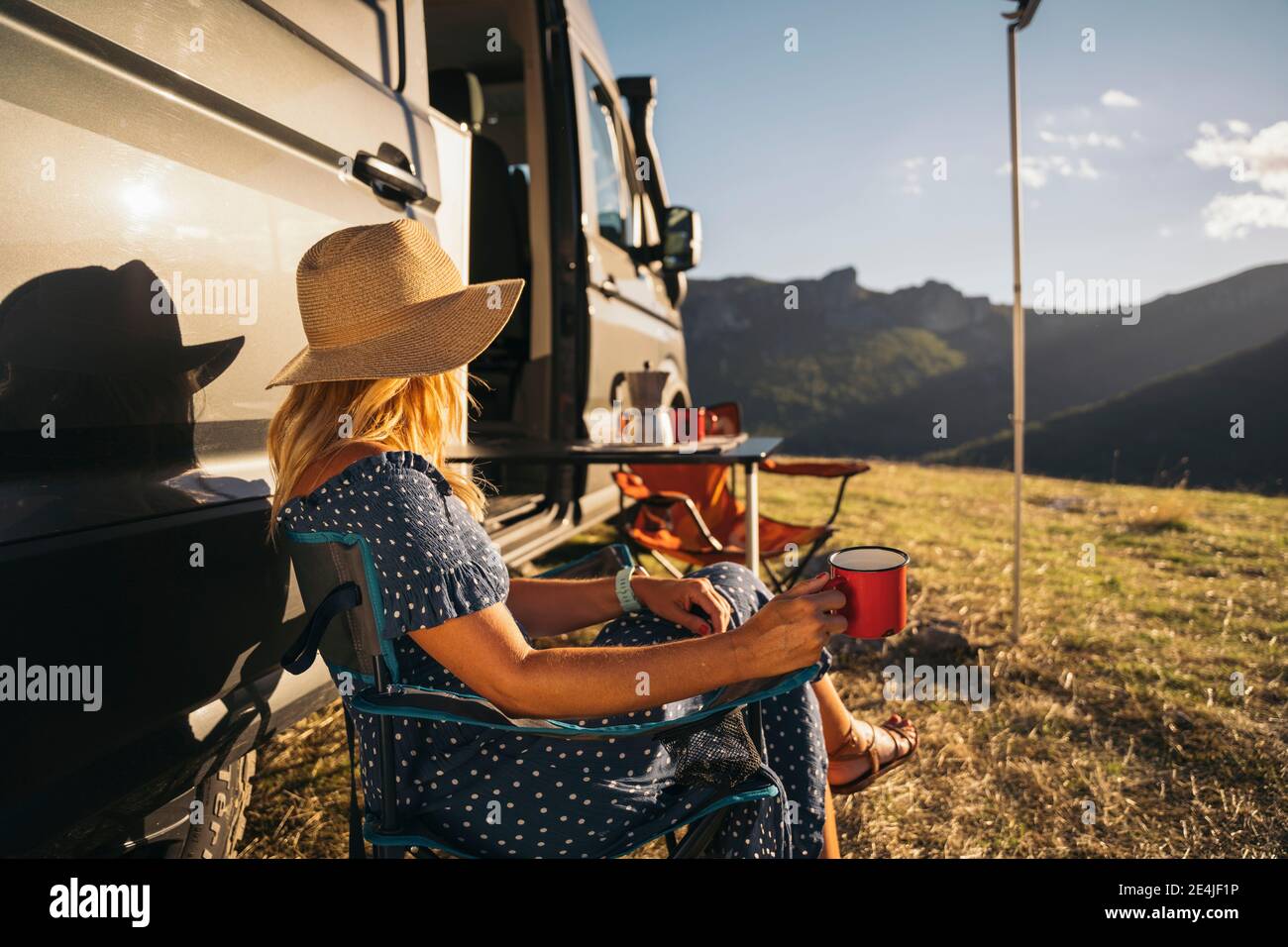 Donna mid adulta che indossa cappello che ha caffè da casa a motore il giorno di sole Foto Stock