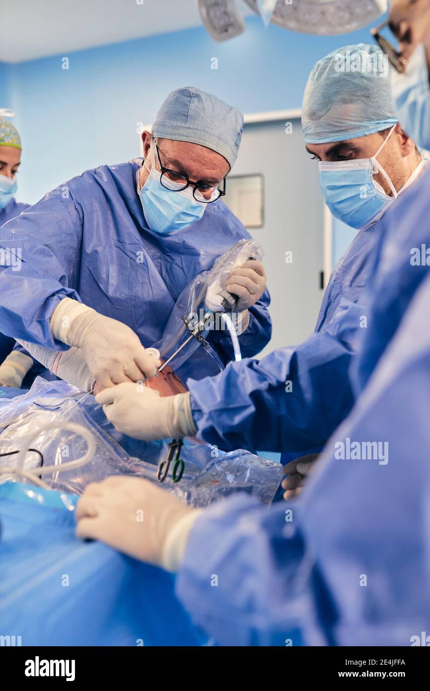 Medico maturo che opera chirurgia artroscopica della spalla con un collega mentre si è in piedi In sala operatoria durante il COVID-19 Foto Stock
