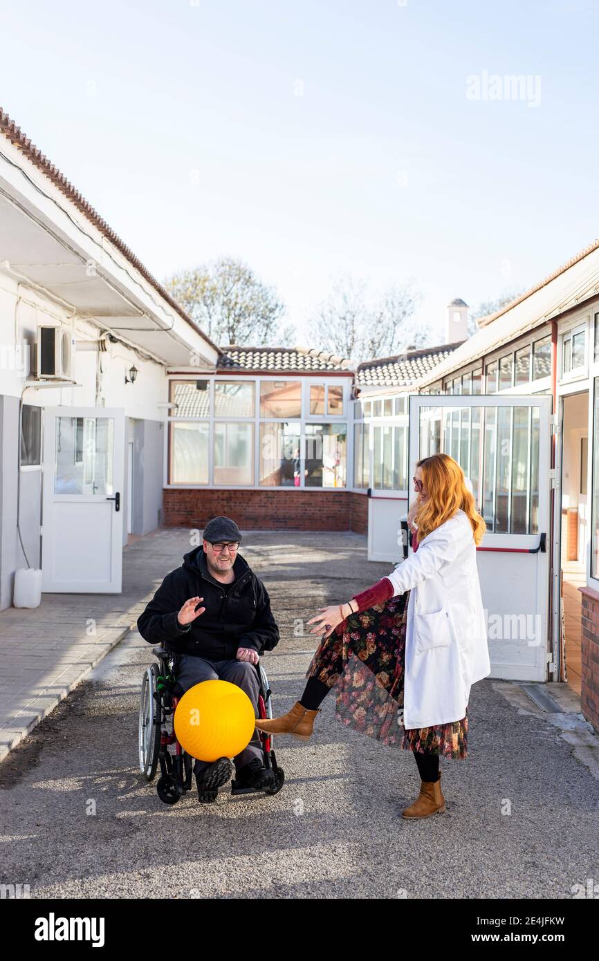 Uomo disabile e infermiera femminile che gioca con la palla fuori riabilitazione centro Foto Stock