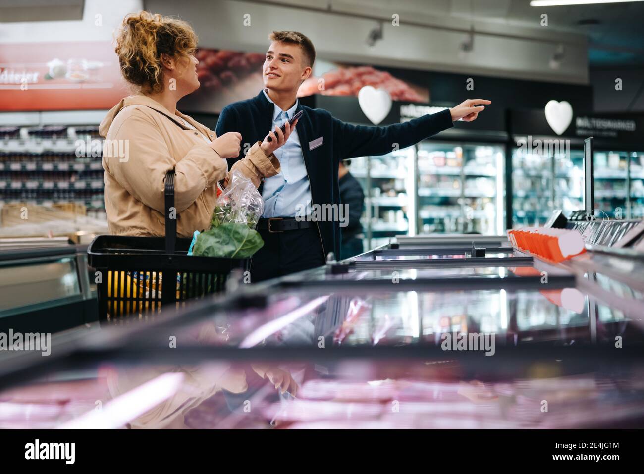 Dipendente del supermercato che dirige l'acquirente verso una corsia. Cliente che chiede di aiutare un dipendente in formazione. Foto Stock