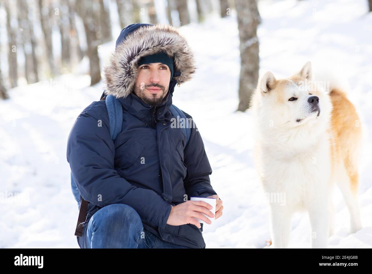 Uomo medio adulto e cane akita guardando via mentre teneva in mano tazza di caffè nella neve Foto Stock