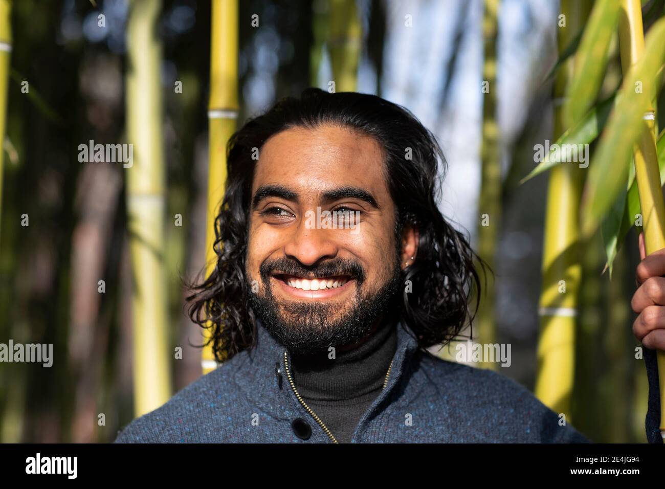 Primo piano di un giovane sorridente bearded che guarda via contro il bambù alberi Foto Stock