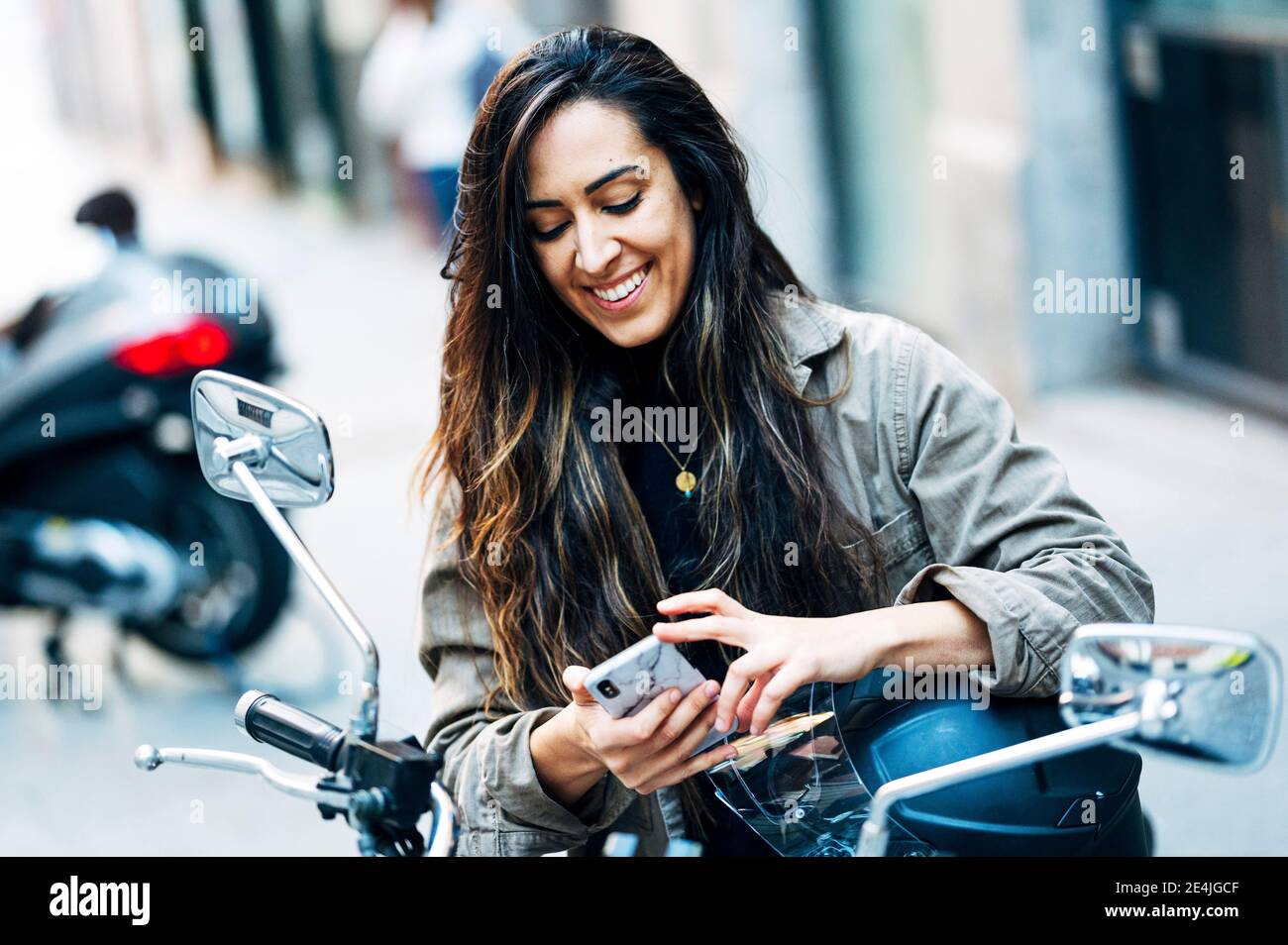 Felice motociclista femminile con casco seduto sul motociclo a lato della città Foto Stock