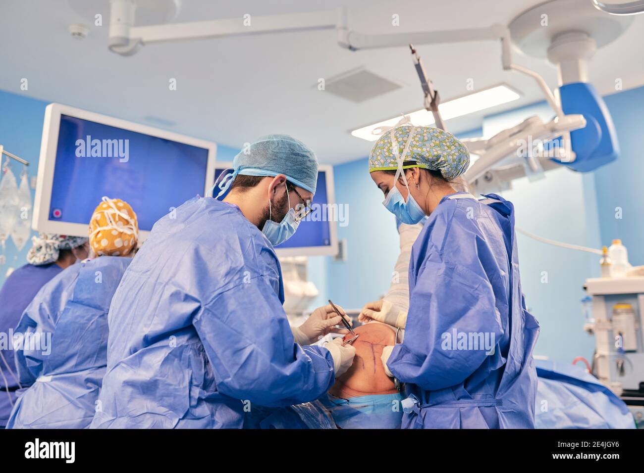 I medici indossano la maschera chirurgica operativa mentre si levano in piedi con il collega in background nella sala operatoria Foto Stock