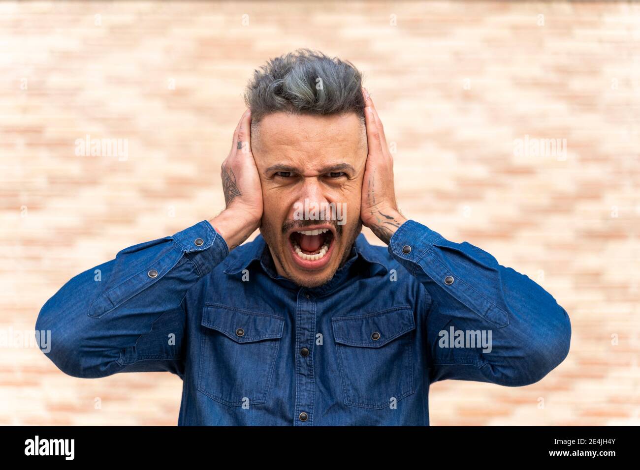 Uomo frustrato coprendo le orecchie mentre gridando contro il muro Foto Stock