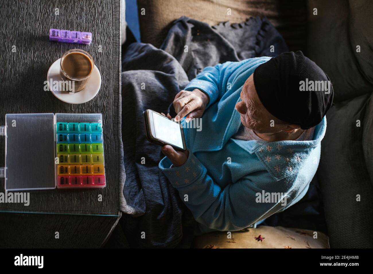 Donna anziana che usa lo smartphone seduto con la tazza di caffè a. tavolo in soggiorno Foto Stock
