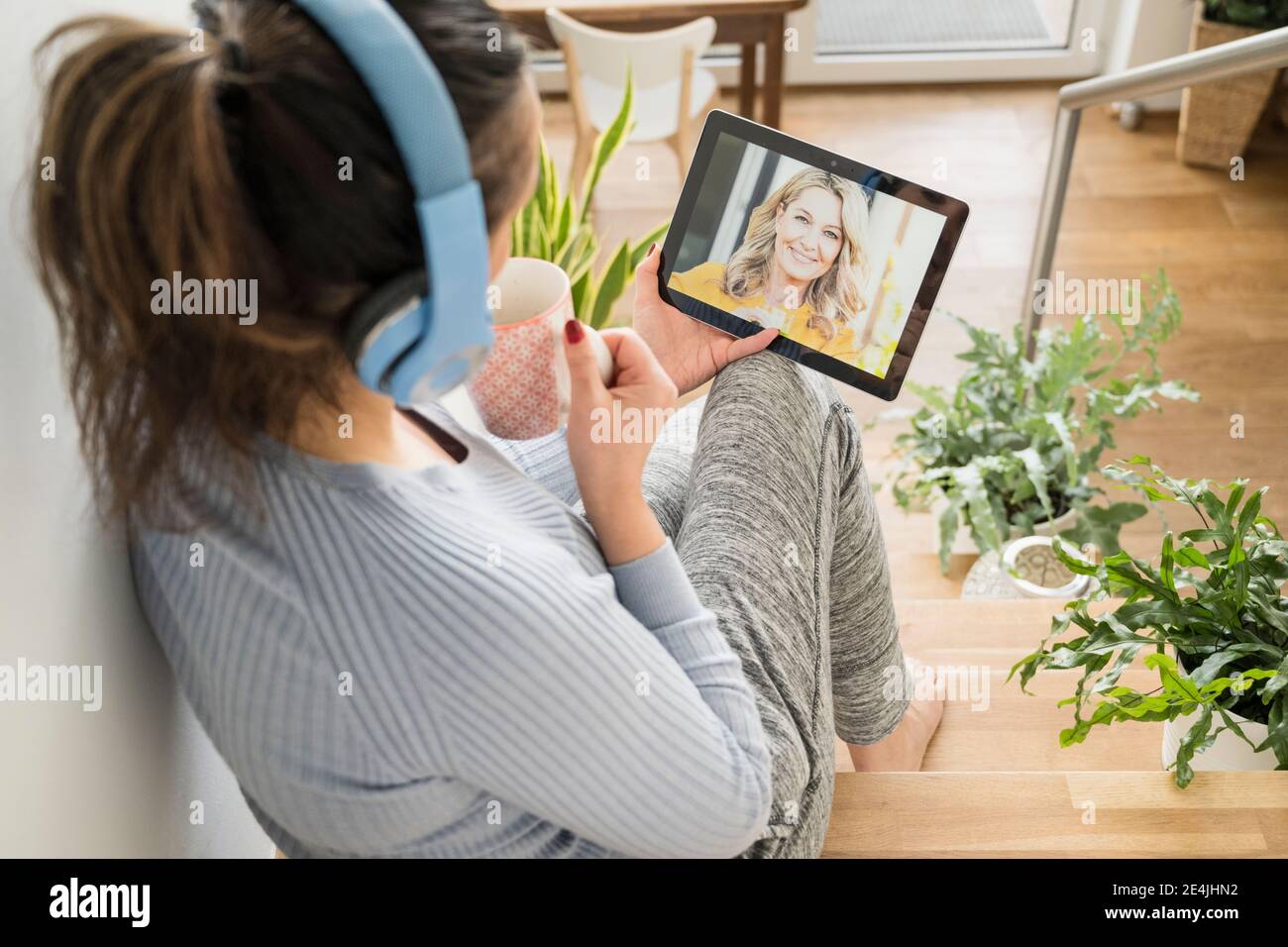 Donna matura che ha il caffè mentre fa la videochiamata su digitale tablet a casa Foto Stock