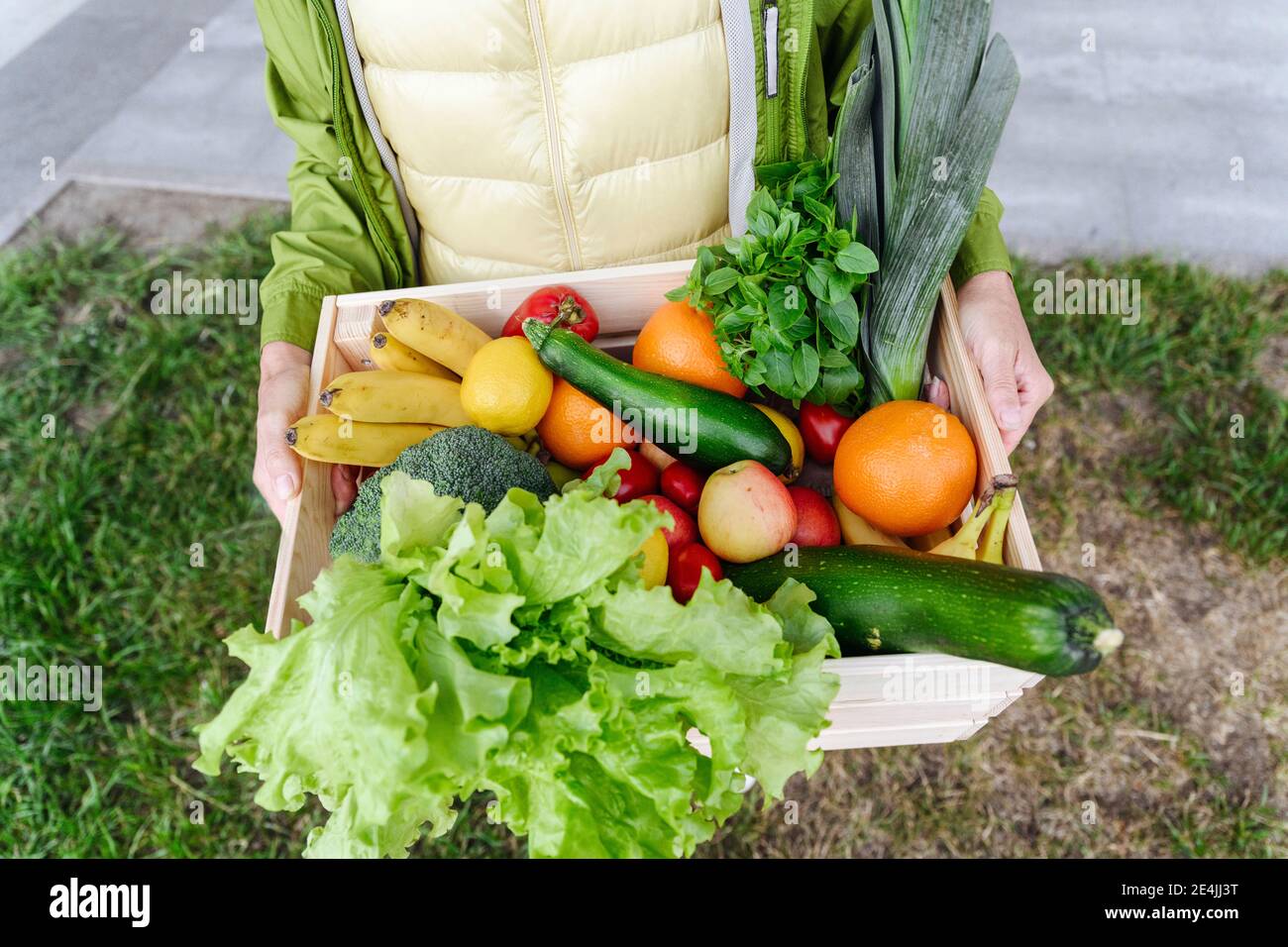 Donna matura con cassa di legno riempita con cibo sano sopra erba Foto Stock