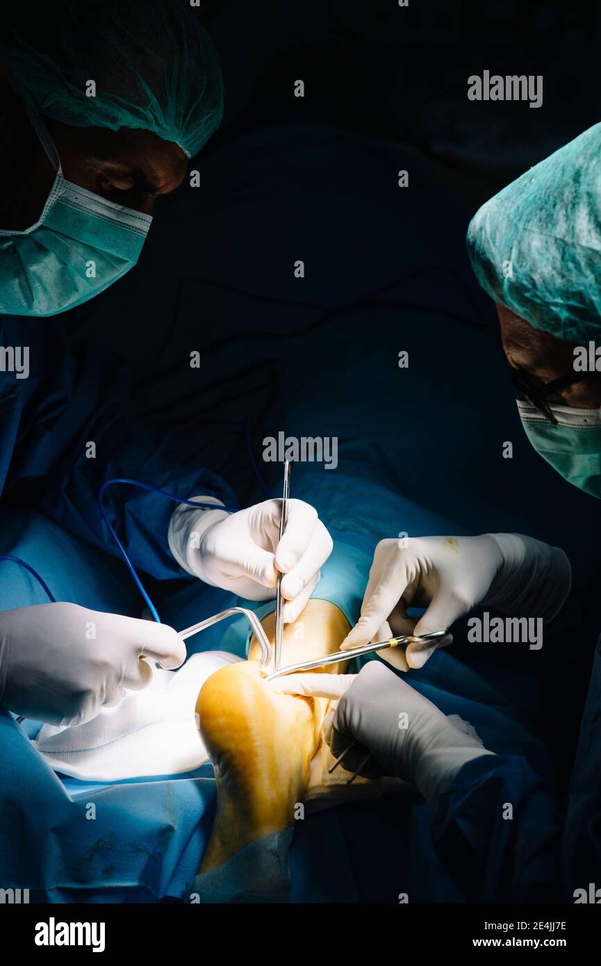 Chirurgo di sesso maschile che passa l'attrezzatura medica durante l'intervento chirurgico in sala operatoria Foto Stock