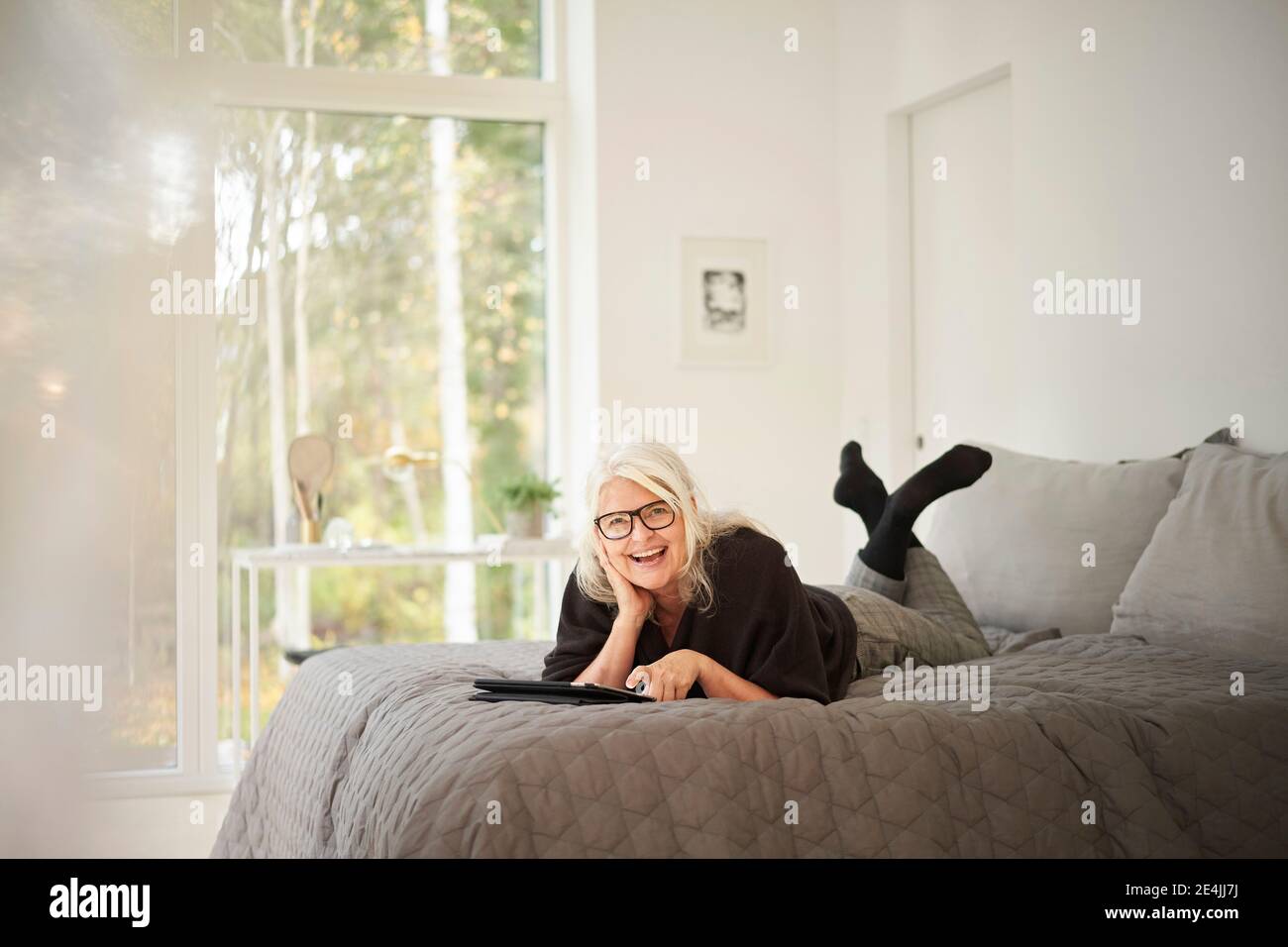 Donna anziana felice con tablet digitale sdraiato sul letto camera da letto Foto Stock