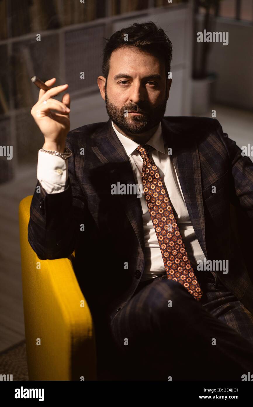 Ritratto di uomo bearded seduto in poltrona con sigaro in mano Foto Stock