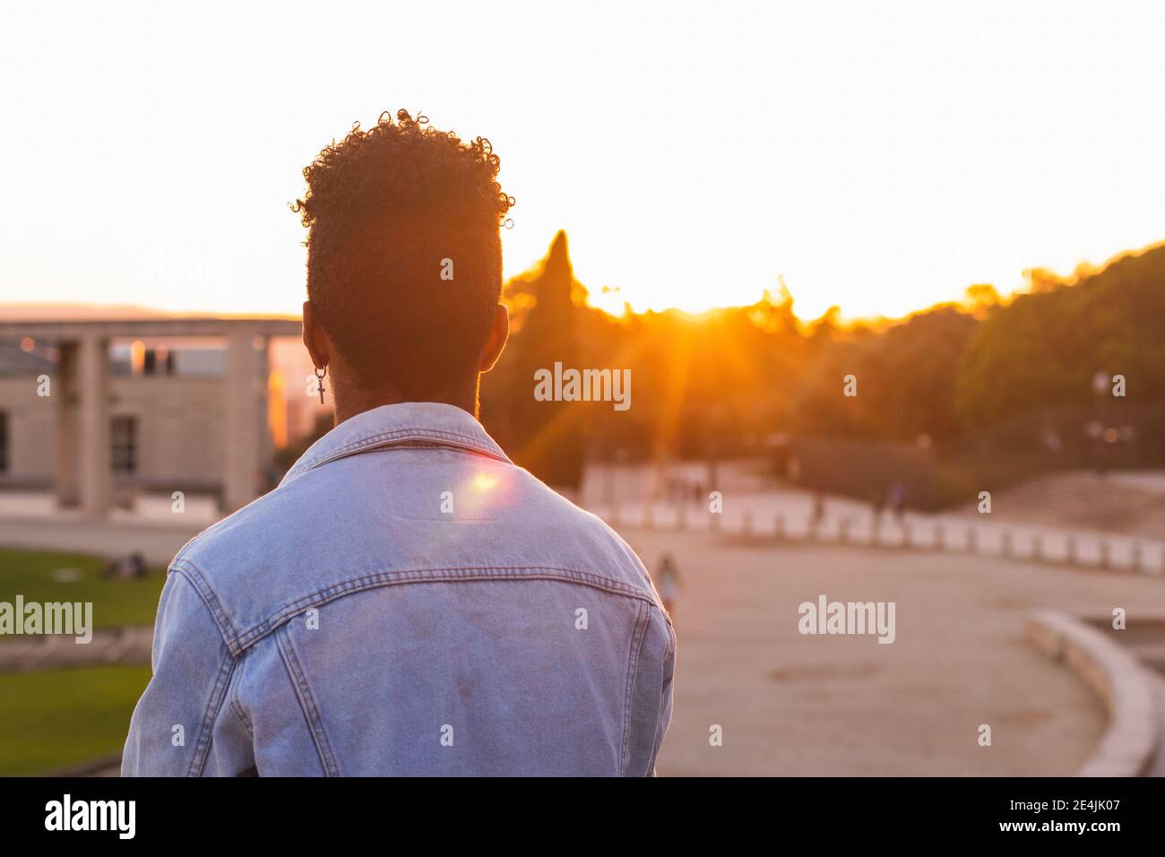 Giovane uomo che indossa una giacca in denim in piedi nel parco durante il tramonto Foto Stock