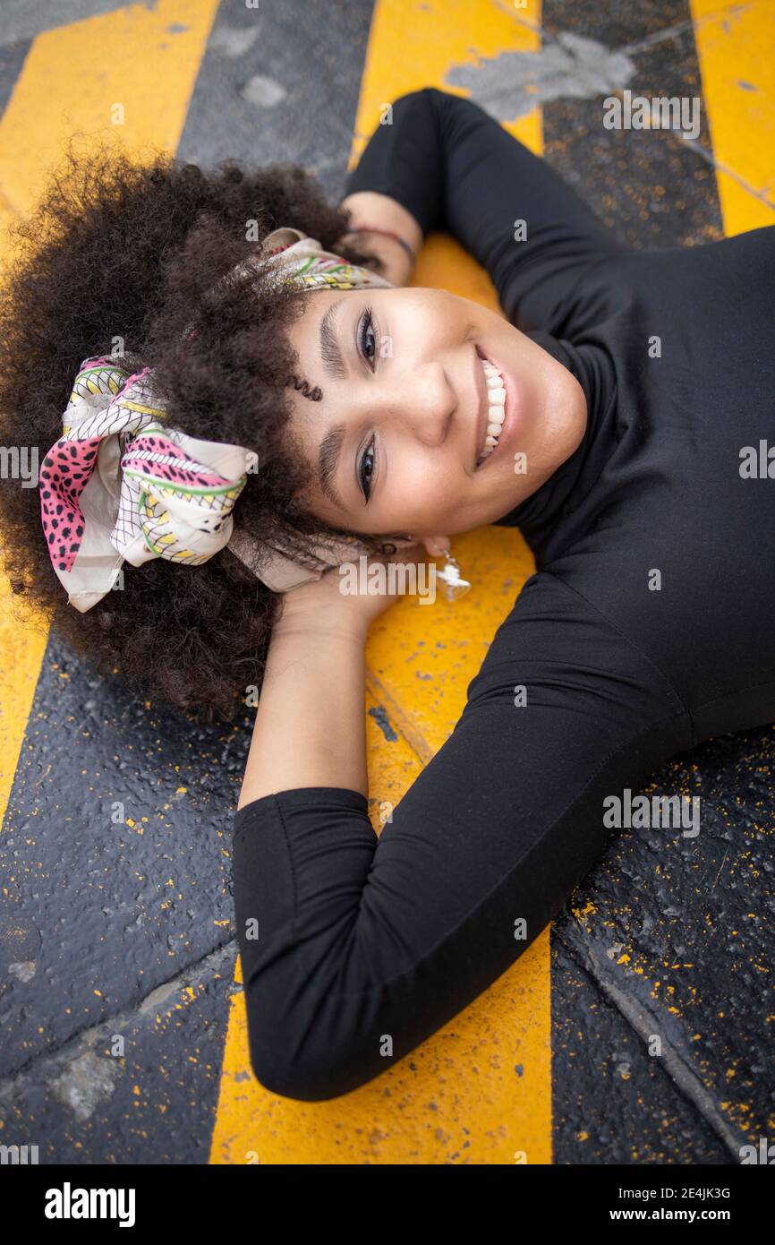Afro giovane donna con le mani dietro la testa adagiata su una strada gialla Foto Stock