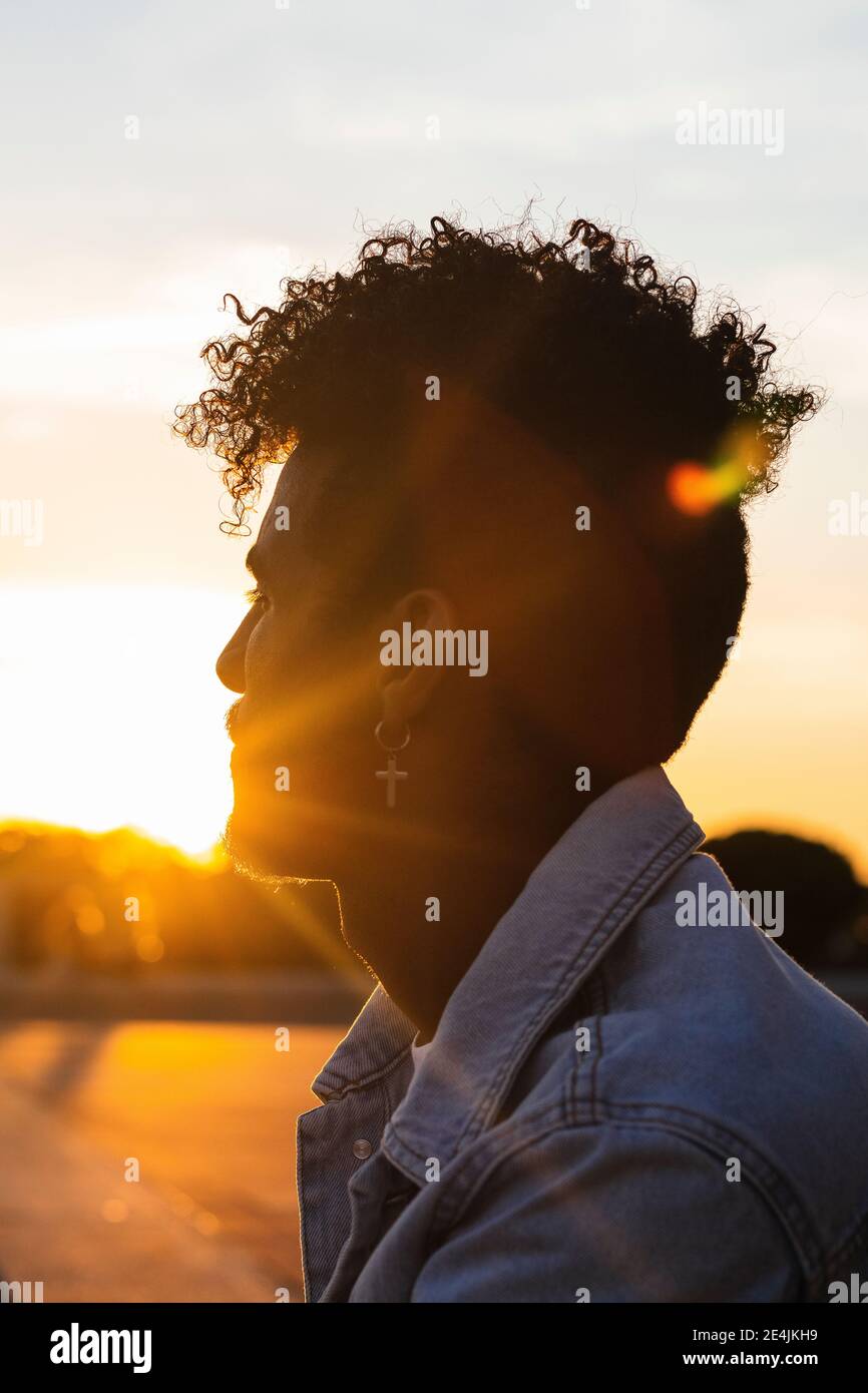 Primo piano di un giovane uomo che indossa orecchini a croce contro il cielo durante il tramonto Foto Stock