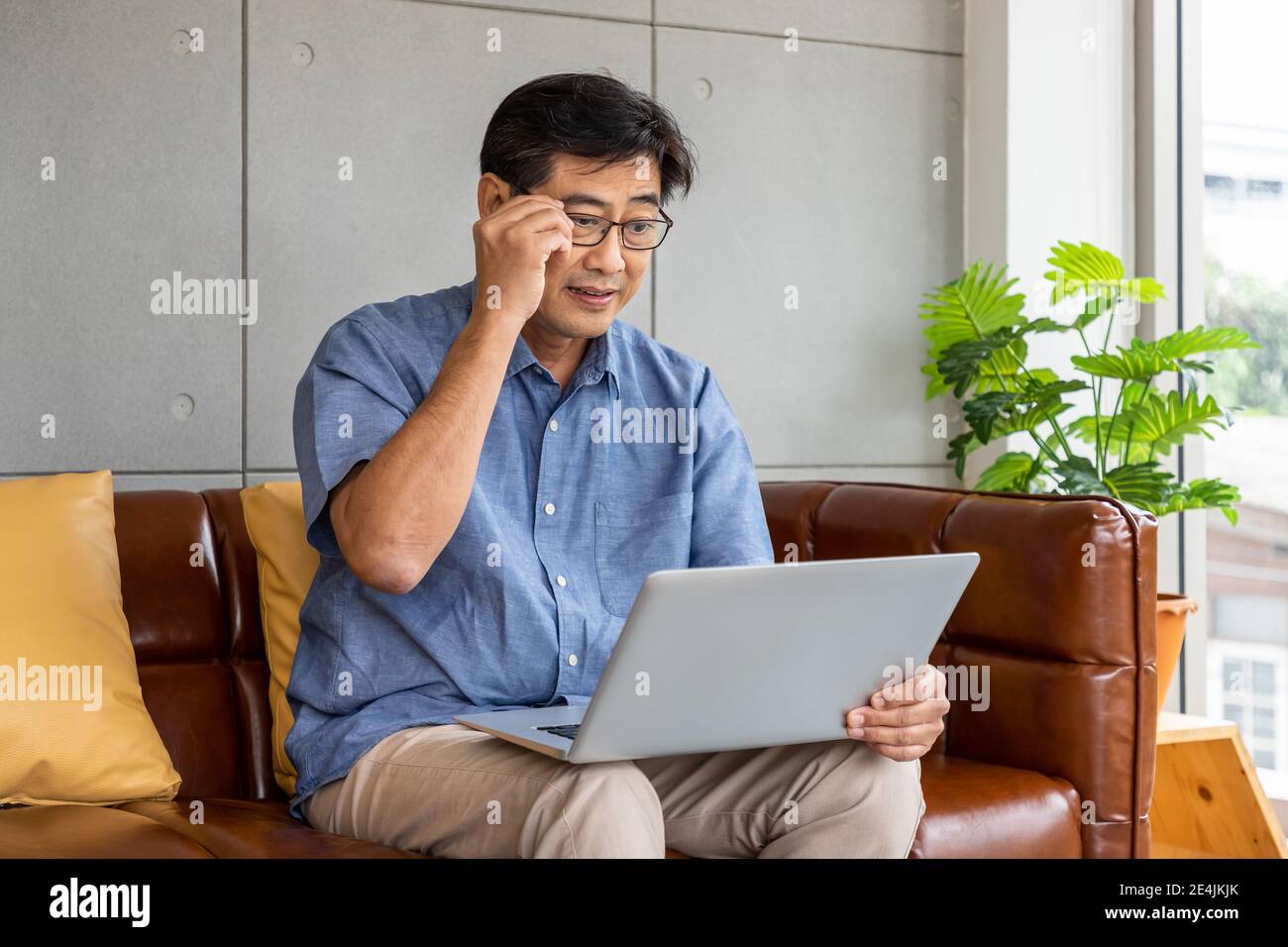 Felice asiatico anziano pensionato uomo seduto sul divano, utilizzando un computer portatile Foto Stock