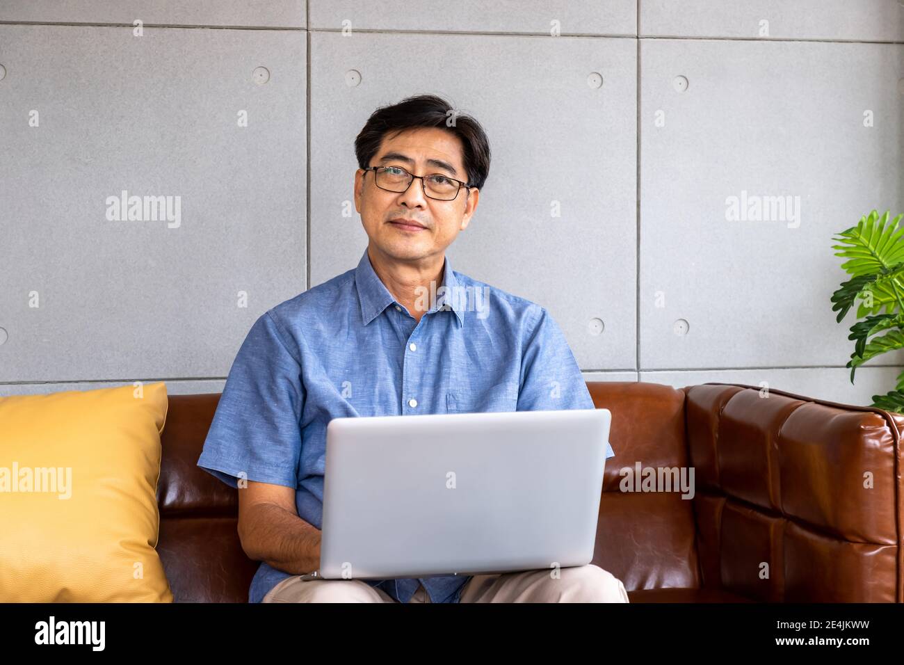 Felice asiatico anziano pensionato uomo seduto sul divano, utilizzando un computer portatile Foto Stock