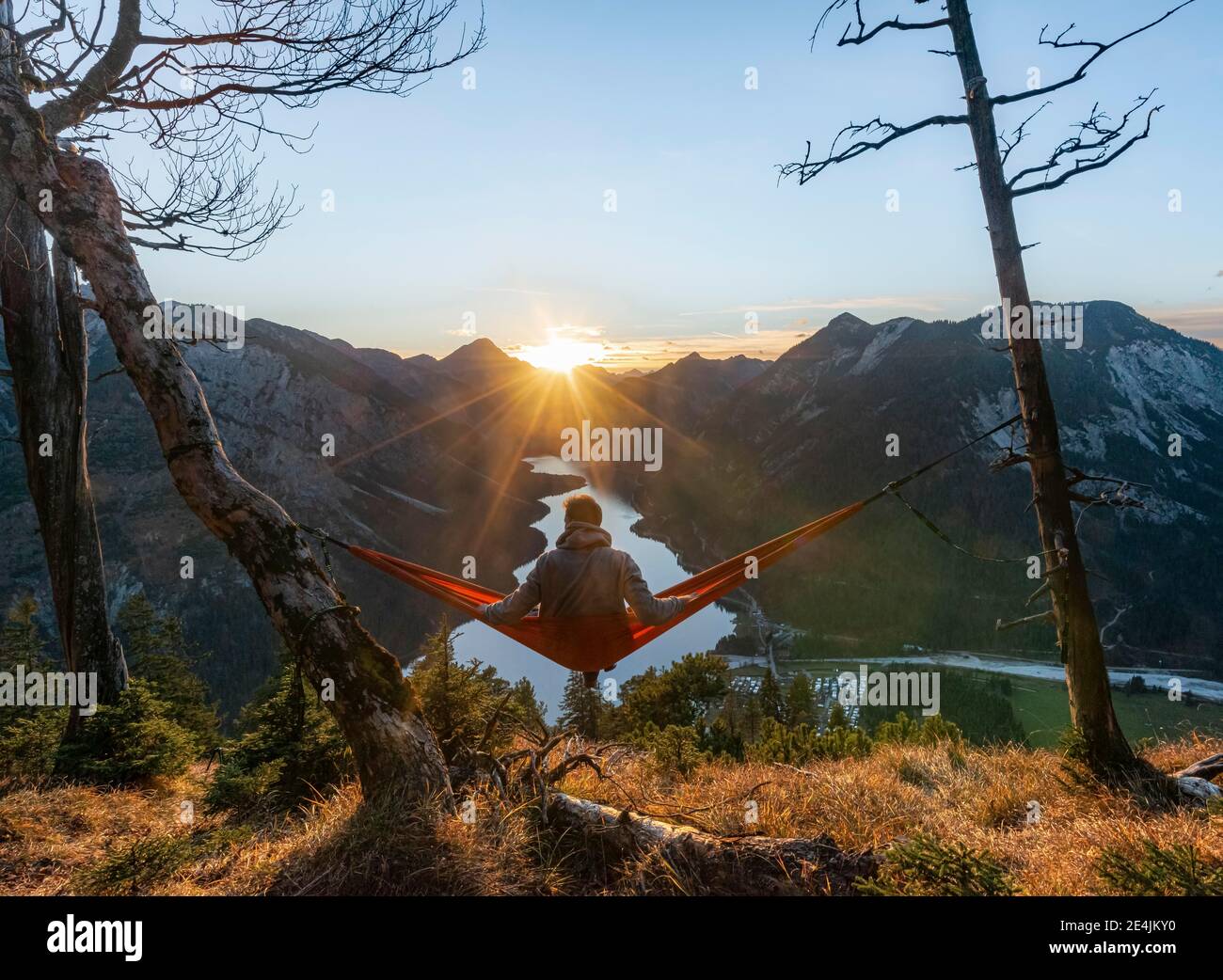 Giovane seduto in un'amaca rossa, vista panoramica sulle montagne con lago, stella solare, tramonto, Plansee, Tirolo, Austria Foto Stock