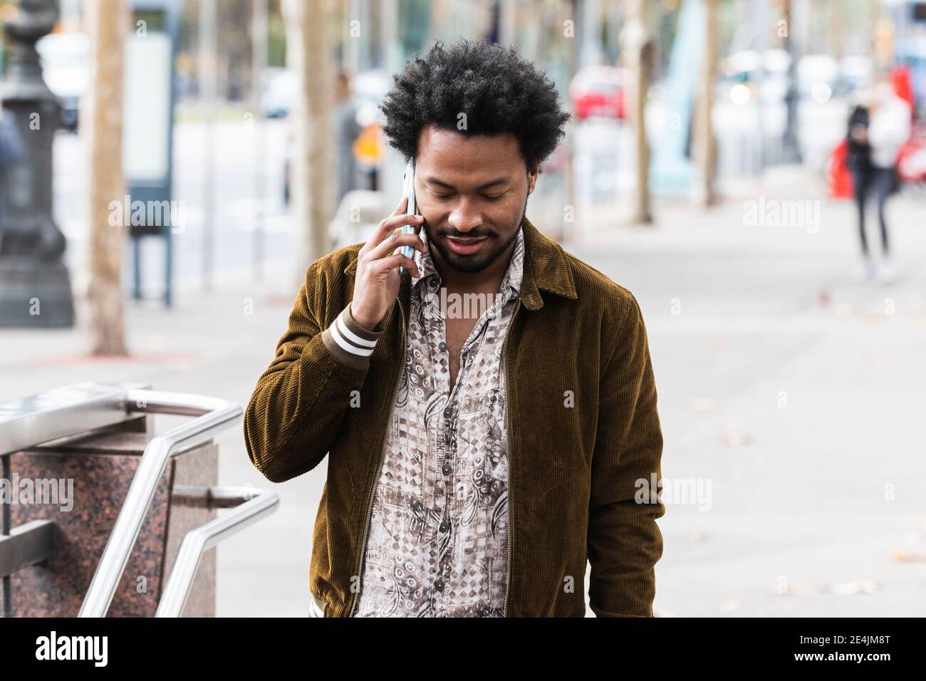 Uomo con capelli afro che comunica con lo smartphone mentre si è in piedi sul sentiero Foto Stock