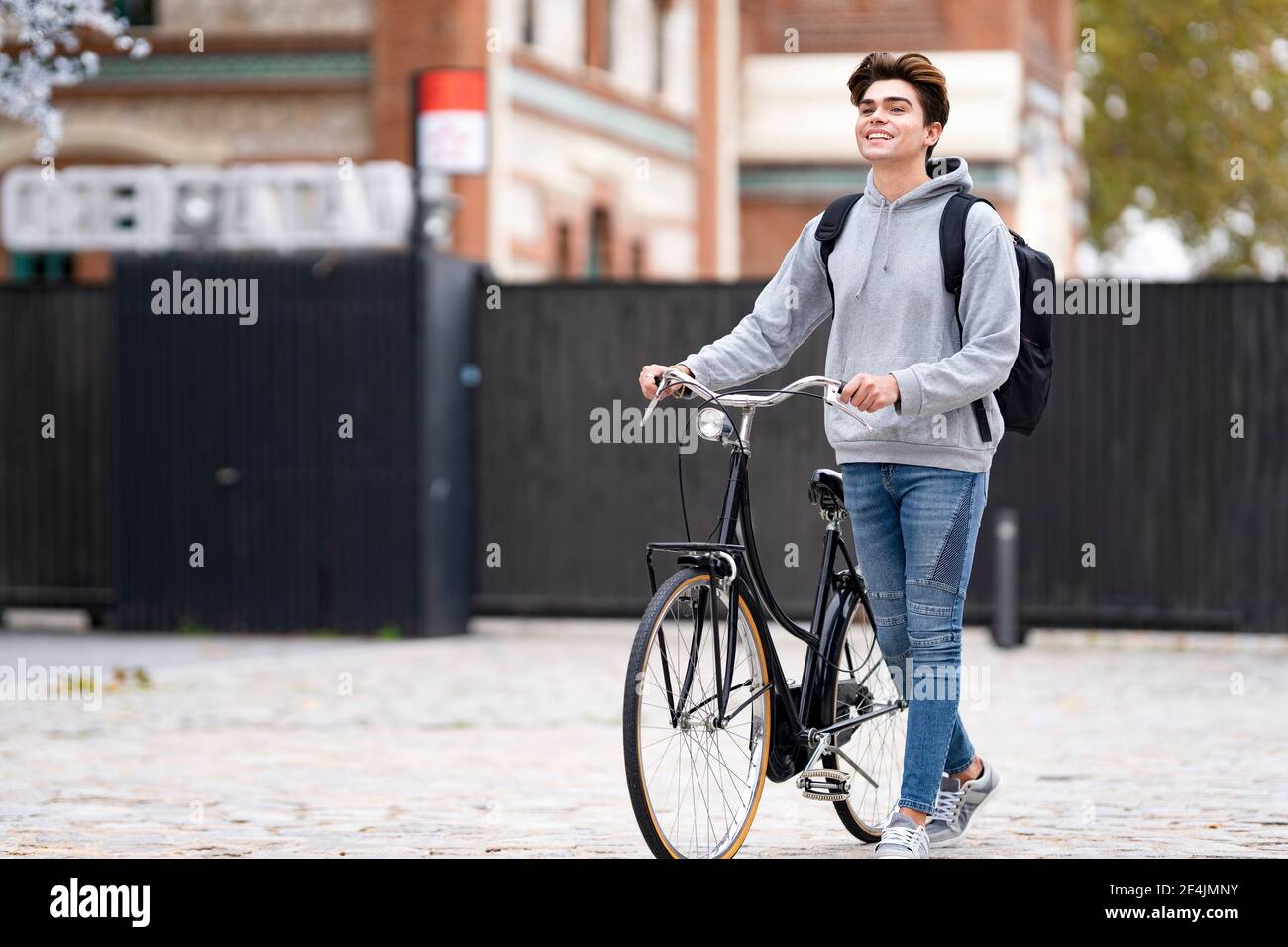 Sorridente giovane alla moda con zaino in bicicletta sul sentiero in città Foto Stock