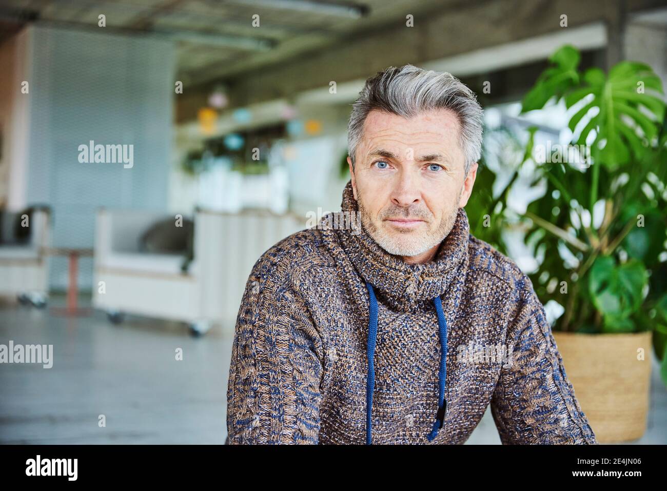 Uomo maturo con gli occhi blu che puntano mentre si siede in ufficio Foto Stock