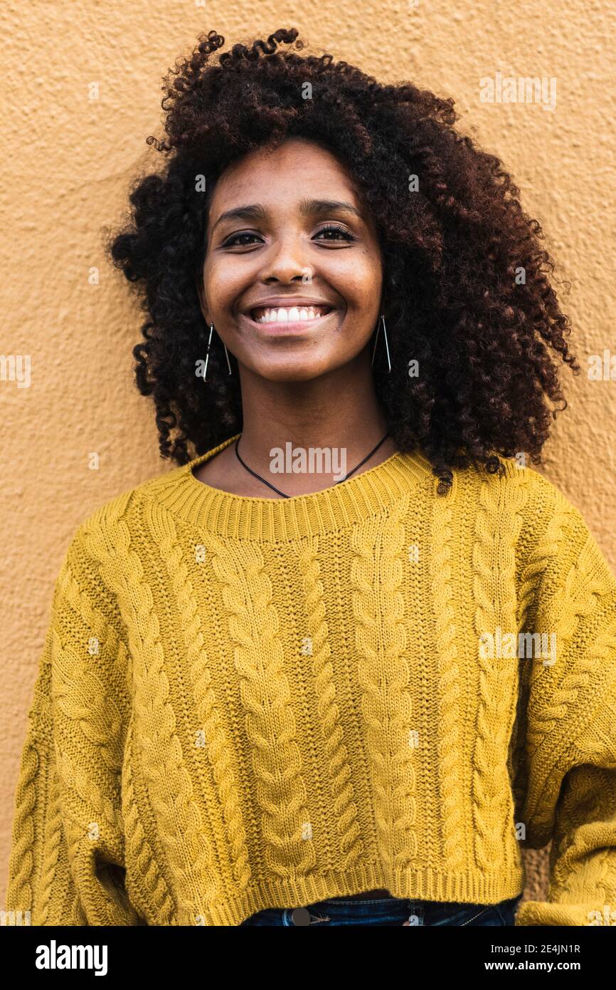 Felice giovane donna in maglione in piedi contro parete gialla Foto Stock
