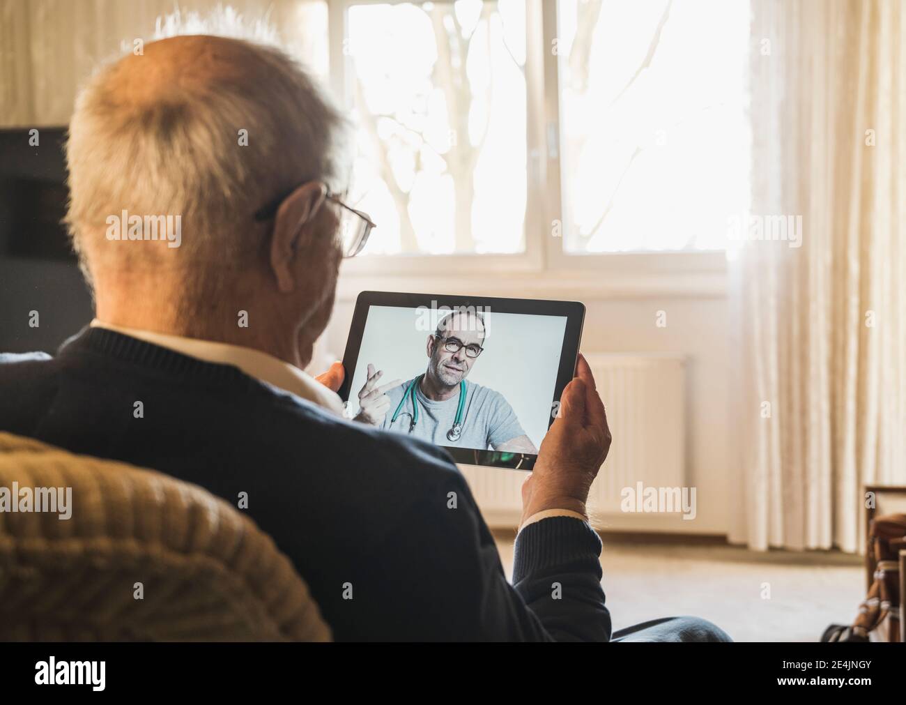 Medico generale maschile che consiglia l'uomo anziano in videochiamata attraverso tablet digitale in salotto Foto Stock
