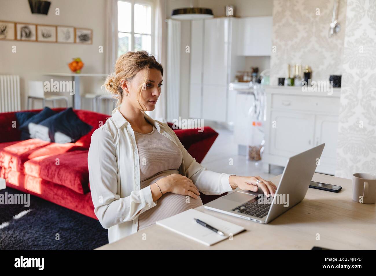 Donna d'affari incinta che lavora su un computer portatile alla scrivania a casa Foto Stock