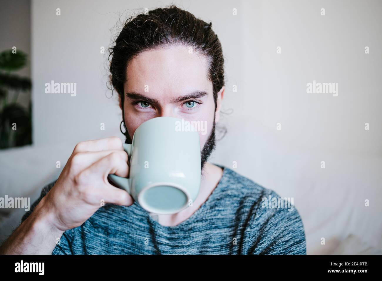 Uomo con gli occhi blu che fissano mentre beve il caffè seduto a. casa Foto Stock